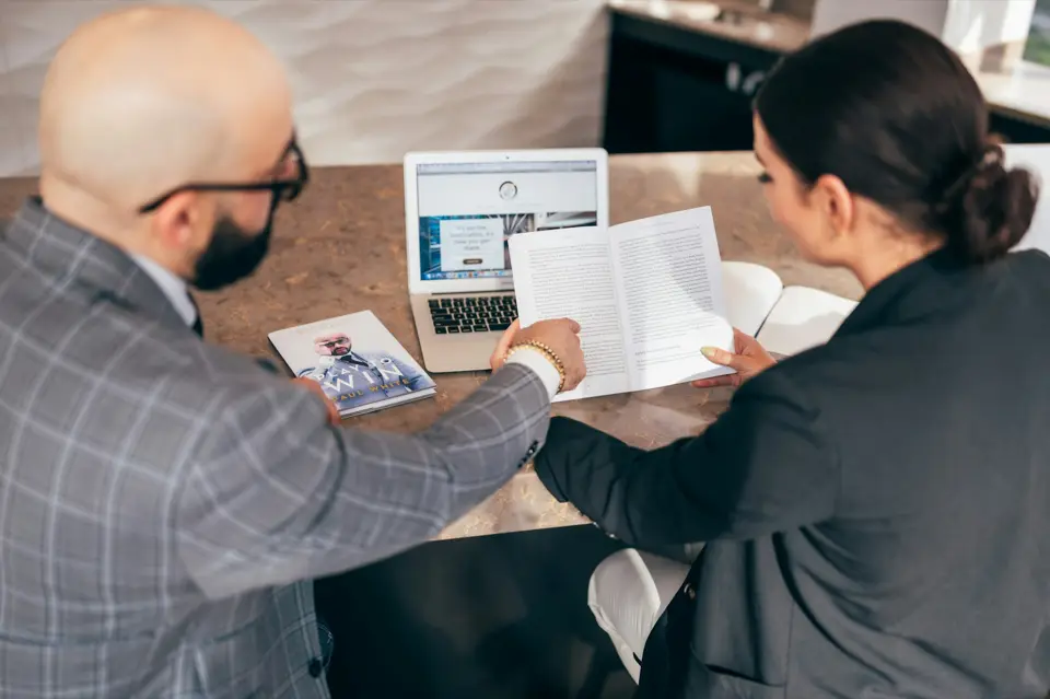 Dos profesionistas revisan un documento junto a una computadora